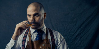 A hipster in a bar apron noses a whisky glass