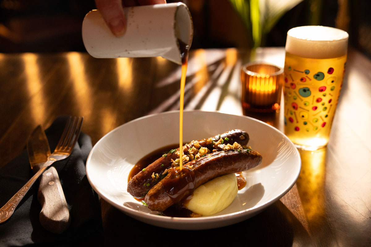 a plate of sausages and mashed potato getting gravy poured over it