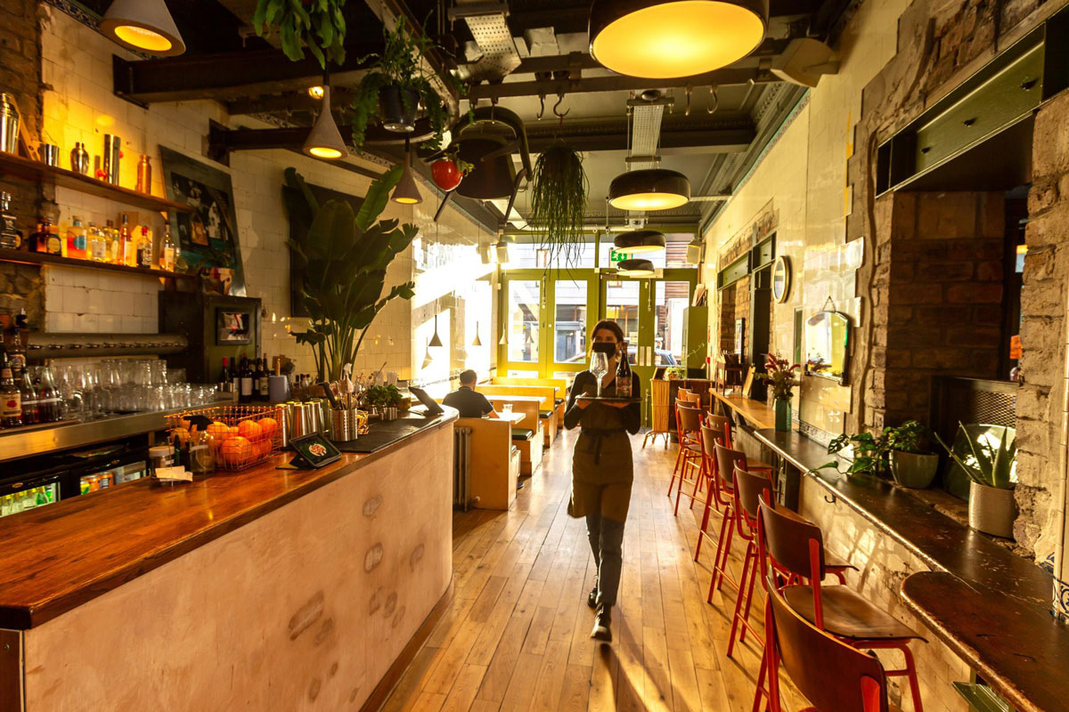 A waitress serves food in a sunlit bar restaurant