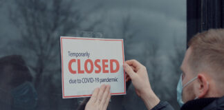 Man wearing medical mask puts a Temporary closed due COVID-19 pandemic sign on a window