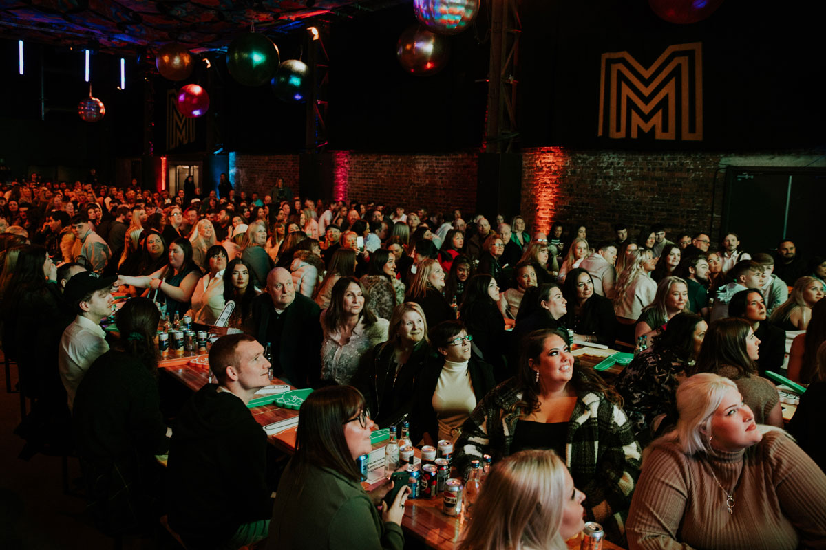 A large function room filled with hundreds of people all looking ip at the stage