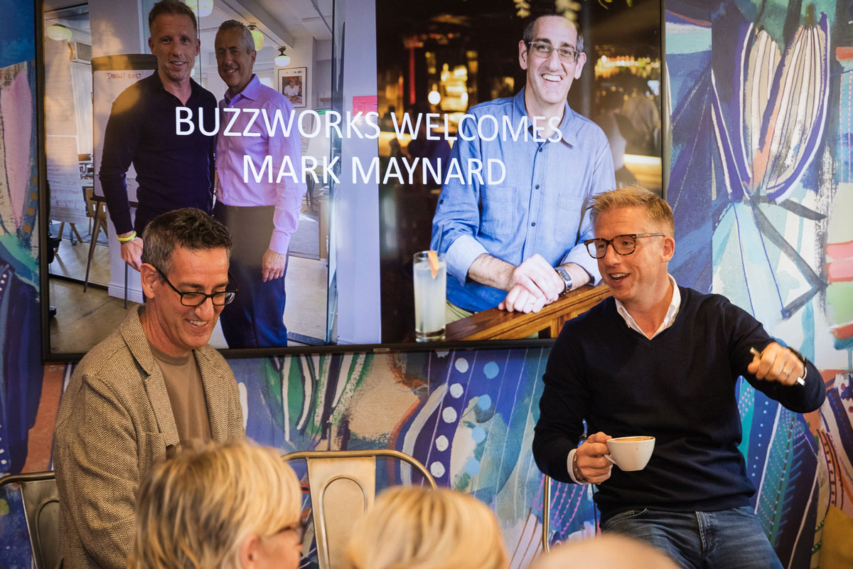 Two middle-aged bespectacled men speak in front of an audience