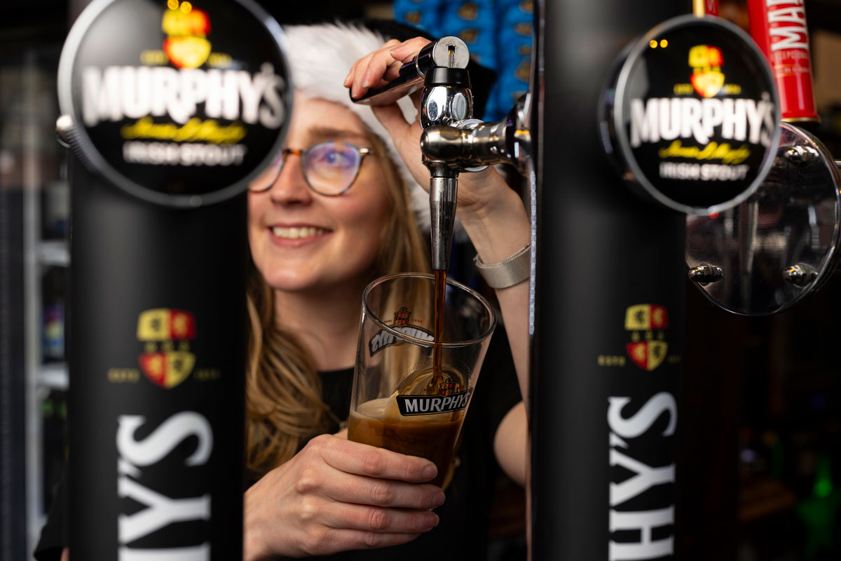 A young woman in a Santa hat pours a pint of stout