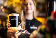 A pint of stout is handed to a customer in a bar