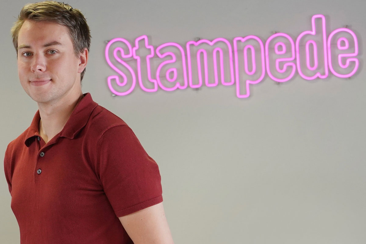 A young tech-bro stands in front of his corporate logo