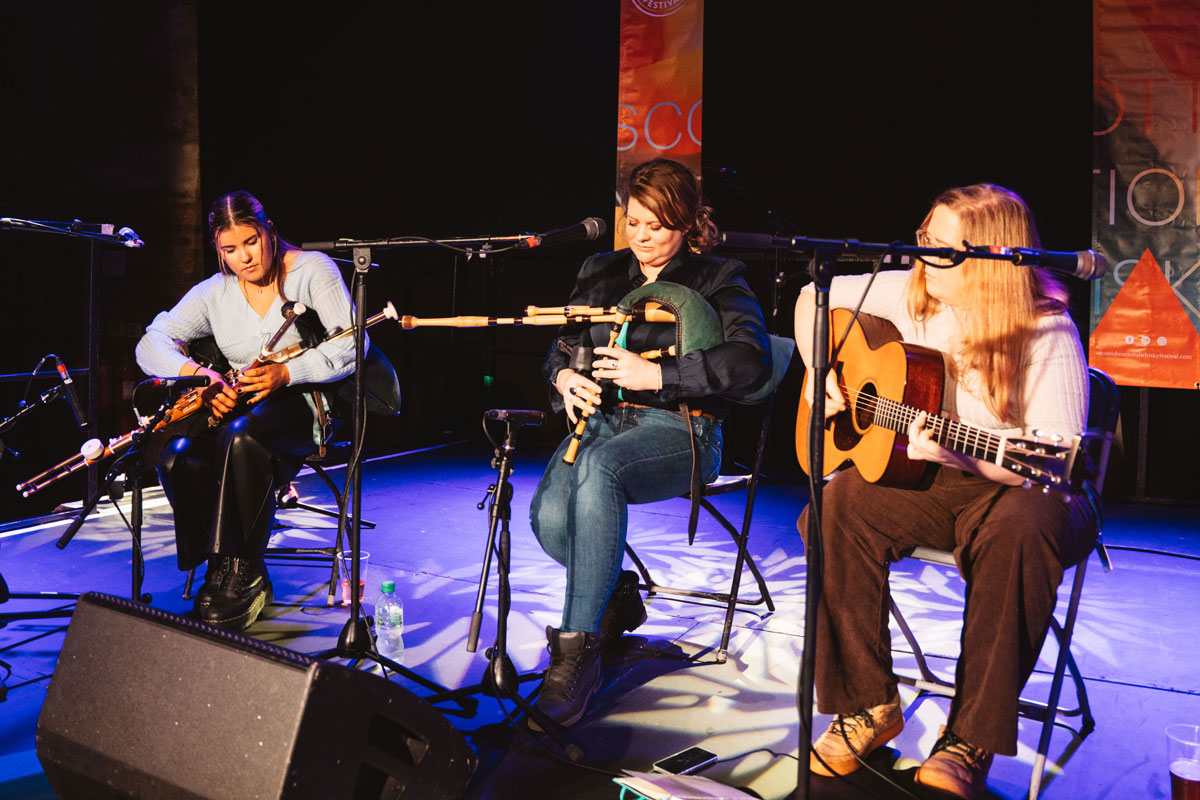 Three ladies sit onstage playing folk music