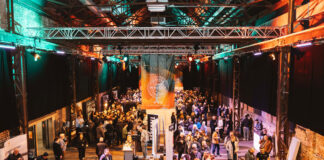 A warehouse style event space full of people and trade stands