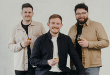 Three entrepreneurial-looking young men smile and raise whisky glasses