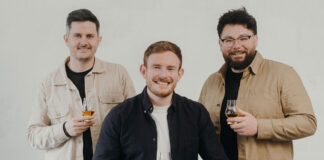 Three entrepreneurial-looking young men smile and raise whisky glasses