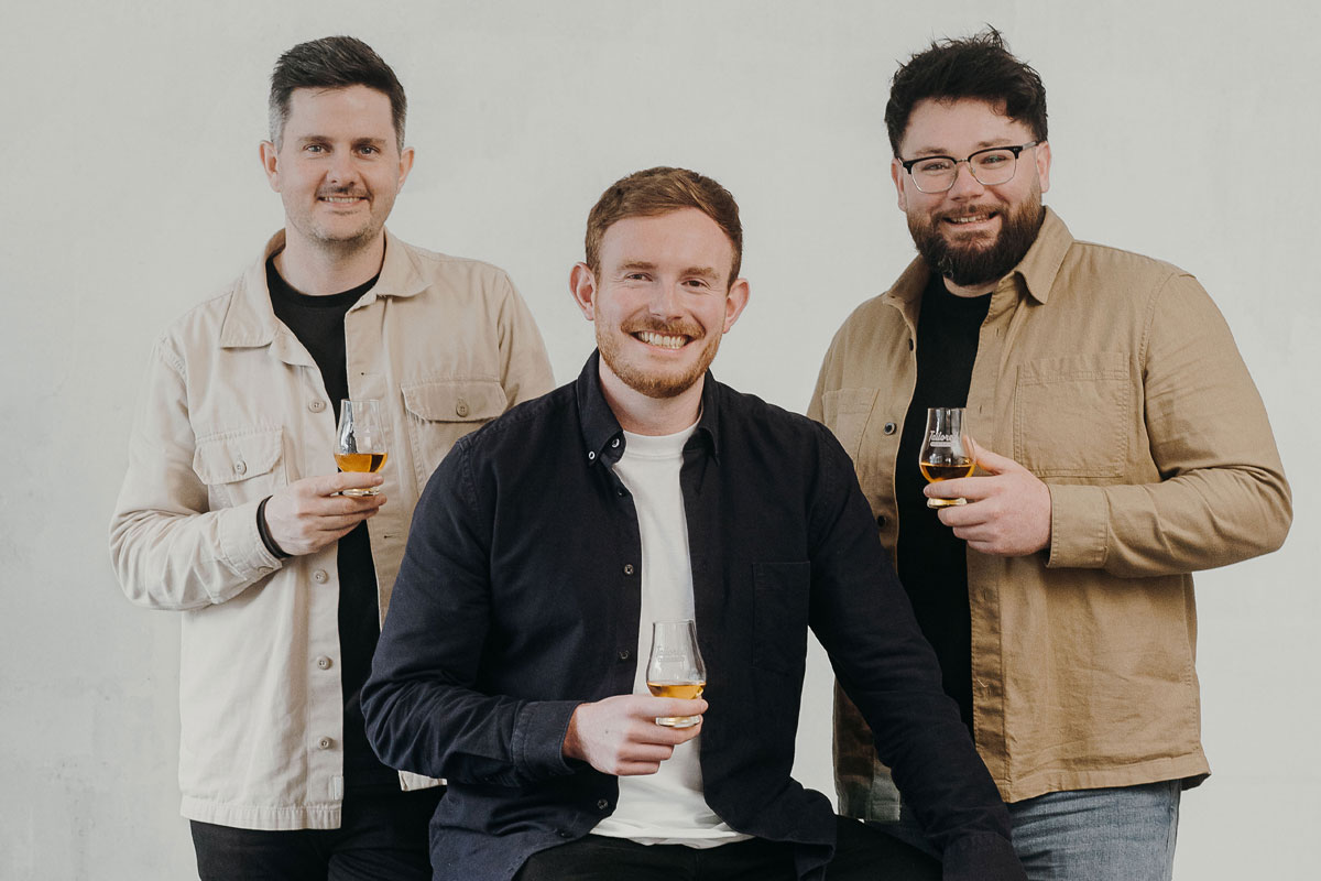 Three entrepreneurial-looking young men smile and raise whisky glasses