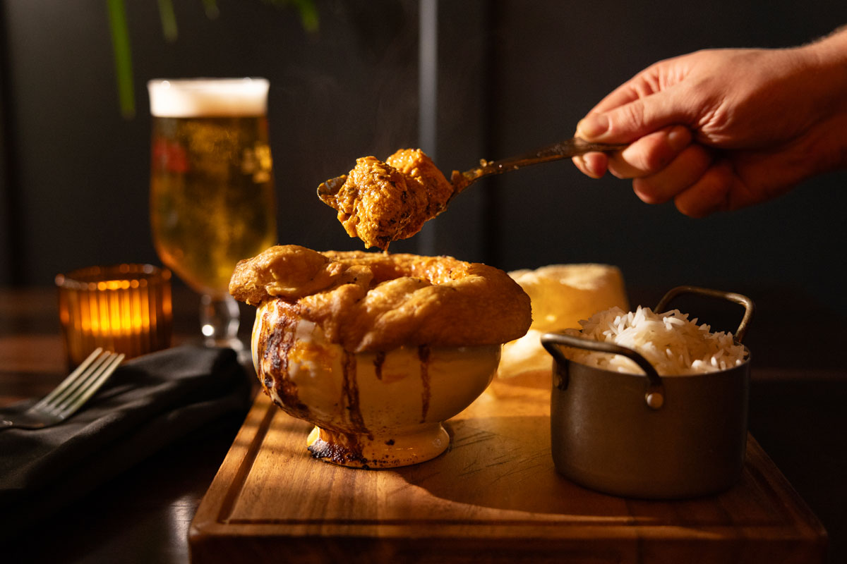 A pastry-topped pie gets broken open to reveal chicken curry inside