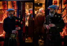Two bagpipe players standing outside a warm looking pub