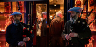 Two bagpipe players standing outside a warm looking pub