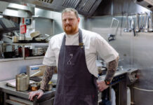 A man in chef's garb stands in a professional kitchen