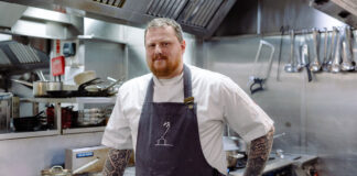 A man in chef's garb stands in a professional kitchen