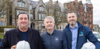 Three businessmen with hard hats stand outside a renovated property
