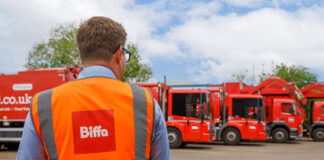 A man in a high-visibility tabard stands in front of a line of lorries