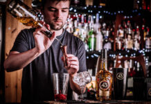 A young barman measures out cocktail ingredients
