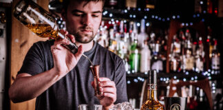 A young barman measures out cocktail ingredients