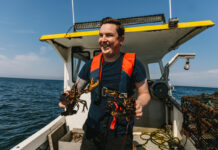 Chef-owner Dean Banks sees opportunity amidst hospitality’s hard times A man, wearing a lifejacket, stands on the open back of a boat at sea, holding a lobster in each hand