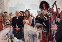 A bride and guests applaud a bagpiper