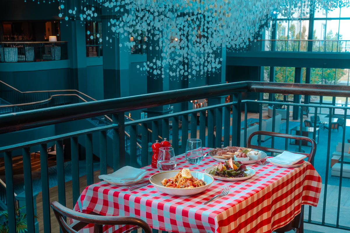 A table dressed for Italian food on a balcony over a larger dining room