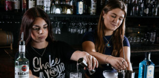Two young women serve behind a bar