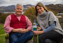A smartly dressed couple sit outdoors with a bottle of spirits