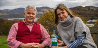 A smartly dressed couple sit outdoors with a bottle of spirits