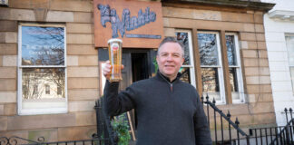 A businessman raises a pint outside a sandstone building