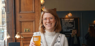 A smiling blonde woman holds up a pint of beer