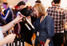 A well-dressed lady noses a glass of wine in a busy room