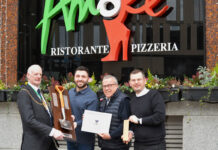 A man wearing a chain of office presents a shiny spade to three men outside a restaurant