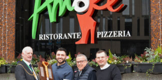 A man wearing a chain of office presents a shiny spade to three men outside a restaurant