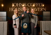 A man cuts a ribbon to open a new building, flanked by a woman on each side