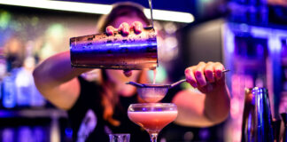 A barperson pours a pink cocktail