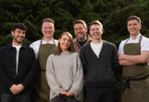 a group of six young hospitality professionals stand outside, smiling