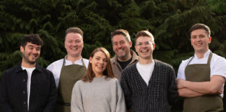 a group of six young hospitality professionals stand outside, smiling