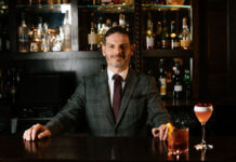 A well-dressed man stands behind an elegant bar