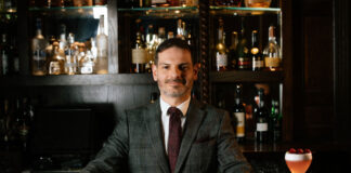 A well-dressed man stands behind an elegant bar