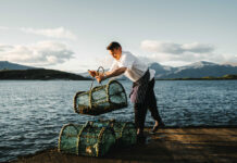 A man in chef's whites stand on a pier with a fishing creel in his hands