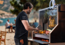 A man cooks meat and vegetables on an outdoor grill