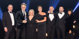 A group of smartly dressed men and women stand on stage to receive an award