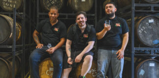 Three casually dressed men in a room full of spirits ageing barrels