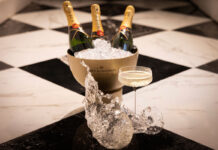 Glasses of champagne on a black and white tiled floor, with an ice bucket full of champagne bottles behind
