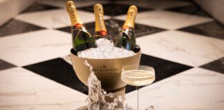 Glasses of champagne on a black and white tiled floor, with an ice bucket full of champagne bottles behind