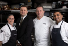 Four hospitality professionals stand in their workwear in a kitchen