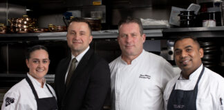 Four hospitality professionals stand in their workwear in a kitchen