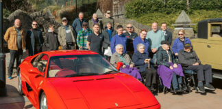 A bright red sports car in the foreground, with people all around, some of them in wheelchairs