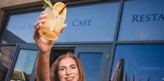 A young woman holds up an iced drink in front of a hospitality venue
